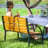 A woman sits on a wooden bench at a table set for a meal outdoors. Anteprima dell’immagine prodotto