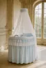 A baby bassinet with a canopy and bedding is set up in a room with large windows and ornate wall moldings. Produktbild-Vorschau