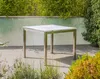 A square table with a marble top and metal legs is set on a paved patio, surrounded by greenery and a frosted glass wall. Produktbild-Vorschau