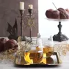 Two glasses of amber liquid sit on a gold tray, with pomegranates and dried foliage in the background. Produktbild-Vorschau
