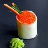 A close-up of a sushi roll with salmon roe, cucumber, and carrot sticks, served with a dollop of wasabi on a dark background. Produktbild-Vorschau
