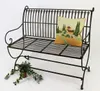 A metal garden bench with a decorative pillow and a small plant. Produktbild-Vorschau