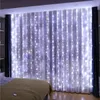 A bedroom with white LED string lights draped over sheer curtains, creating a festive and cozy atmosphere. A bed with a beige blanket is visible in the foreground. Náhled obrázku produktu