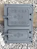 A cast iron stove door with decorative patterns, lying on a bed of gravel and stones. Náhľad obrázku produktu