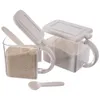 Two clear storage containers with beige lids and handles, filled with light brown powder, and a small beige spoon. Anteprima dell’immagine prodotto