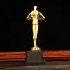 A golden trophy with a black base is displayed against a black background, with a textured orange fabric behind it. Produktbild-Vorschau