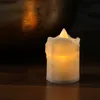 A close-up of a small, battery-operated LED candle with a flickering yellow flame, placed on a wooden surface. A large, textured metallic object is visible in the background. Produktbild-Vorschau