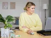 A woman is working on a laptop at a desk with a plant and other items. Produktbild-Vorschau
