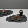 Two black placemats with desserts and a cup of coffee on a light gray and white surface. Produktbild-Vorschau