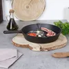 A cast iron pan with ingredients for cooking is placed on a wooden board on a countertop. Produktbild-Vorschau