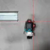 A laser level tool projects red lines onto a gray concrete wall next to a metal track. Produktbild-Vorschau