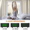 A woman stretching in bed with three digital alarm clocks displayed below, illustrating different brightness levels. Produktbild-Vorschau