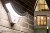 A split image showing a white LED outdoor light with a motion sensor mounted on a brick wall on the left, and a modern house with large windows and exterior lighting on the right. Produktbild-Vorschau