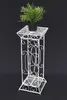 A white metal plant stand with a potted green plant on top, set against a black background. Náhled obrázku produktu