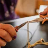 A person's hands are using pliers to manipulate a gold-colored chain. Produktbild-Vorschau