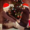 A couple wearing Santa hats sits in front of a decorated Christmas tree. Anteprima dell’immagine prodotto