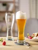 Two beer glasses, one filled with beer and foam, and the other empty, sit on a wooden table with radishes and a plate of food in the background. Produktbild-Vorschau