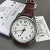 A close-up of a Casio analog watch with a brown leather strap, placed on a gray surface next to some documentation. Produktbild-Vorschau