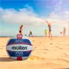 A volleyball on a sandy beach with people playing volleyball in the background. Anteprima dell’immagine prodotto