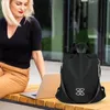 Schwarzer Rucksack mit silbernem Zieremblem auf der Vorderseite, neben einer Frau, die auf einer Holzbank einen Laptop benutzt Produktbild-Vorschau