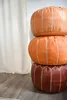 Three stacked leather poufs in different shades of brown and orange, placed next to a cream-colored curtain. Voir les images du produit