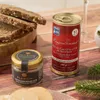 A still life arrangement of gourmet food products, including a can of foie gras, a jar of truffles, and slices of bread, set on a wooden surface with festive greenery. Produktbild-Vorschau