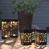 Several decorative solar lanterns are placed on a wooden surface, casting intricate light patterns. A potted plant is visible in the background. Podgląd zdjęcia produktu