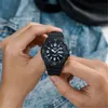 Hands holding a black Casio watch against a denim background. Voir les images du produit