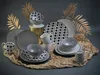 A collection of black and white patterned dinnerware, including plates, bowls, and mugs, arranged on a textured surface with decorative gold leaves in the background. Produktbild-Vorschau