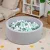 A round ball pit filled with colorful balls, placed on a rug in a child's room next to a bed and a shelf unit. Produktbild-Vorschau