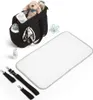 A black diaper bag with various baby accessories laid out around it, including a changing mat, a stuffed animal, a baby bottle, and straps. Produktbild-Vorschau