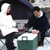 A couple is sitting in front of a tent in the snow, with a cooler between them. Náhled obrázku produktu