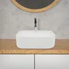 A white ceramic vessel sink with a chrome faucet is placed on a wooden countertop above white cabinets, with a concrete wall and a round mirror in the background. Produktbild-Vorschau
