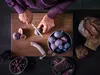 A person is preparing food, slicing figs on a wooden cutting board, with bread, olives, and sausage nearby. Voir les images du produit