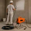 A person is using a paint sprayer in a room with concrete walls. Produktbild-Vorschau