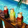 Three perfume bottles are displayed on a wooden railing next to a swimming pool. Voir les images du produit