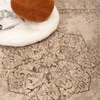 A close-up view of a rug with a decorative pattern, featuring a white cushion and a brown pillow. Voir les images du produit