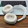 A pair of white headphones rests on a laptop keyboard, with the headphones also partially on a wooden surface. Podgląd zdjęcia produktu