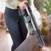 A person is using a cordless vacuum cleaner on a wooden table. Voir les images du produit