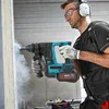 A man is using a cordless hammer drill to drill into a concrete wall, creating dust. Voir les images du produit