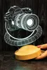 A 3D LED lamp shaped like a camera sits on a wooden base. Produktbild-Vorschau
