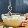 A person is using a hand mixer to mix batter in a glass bowl. Produktbild-Vorschau