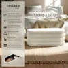 A white upholstered ottoman is placed on a textured rug in front of a bed with white linens. Text overlays describe the product's features. Produktbild-Vorschau