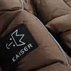 A close-up of a brown quilted fabric with a black label showing a white logo and the word KAISER. Produktbild-Vorschau