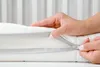 A close-up shot of a person's hands zipping up a white mattress topper with a gray zipper. Náhľad obrázku produktu