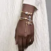 A close-up shot of a person's wrist wearing multiple charm bracelets. Produktbild-Vorschau