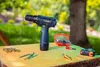 A cordless drill and accessories are laid out on a wooden surface outdoors. Podgląd zdjęcia produktu