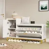 A white shoe cabinet with a padded seat and gold metal legs, featuring multiple storage compartments and drawers. Several pairs of shoes are neatly arranged on the floor in front of the cabinet. Produktbild-Vorschau