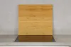 A bamboo cutting board placed over a black glass stovetop on a gray countertop. Produktbild-Vorschau