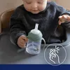 A baby sitting in a high chair, holding a sippy cup with a straw. Produktbild-Vorschau